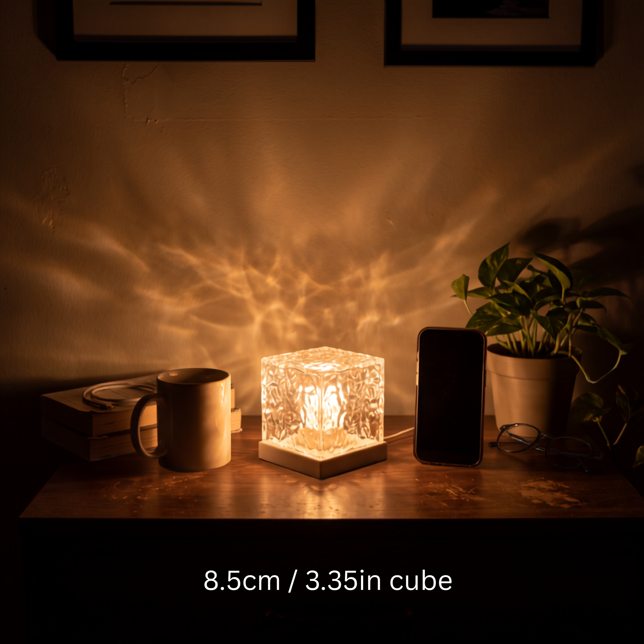 Aurora Cube lamp glowing warm amber on a wooden desk beside a mug and phone, shown at 8.5 cm cube size