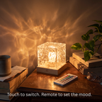 Aurora Cube lamp glowing amber on a desk beside its remote control, switched on by touch