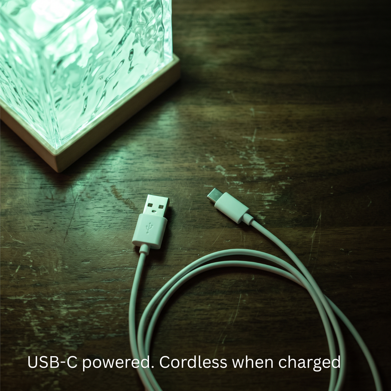 Aurora Cube lamp glowing green on a wooden surface with its USB-C charging cable, cordless once charged