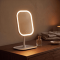 GlowVanity LED makeup mirror glowing warm white on a wooden dresser beside perfume bottles