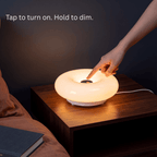 A hand touching the top of the Halo donut lamp to turn it on, holding to dim it