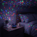 Starlull projector scattering red, green and blue star dots across a dark bedroom from a bedside table