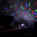 Starlull projector throwing red, green and blue dots across a desk setup with a monitor and keyboard