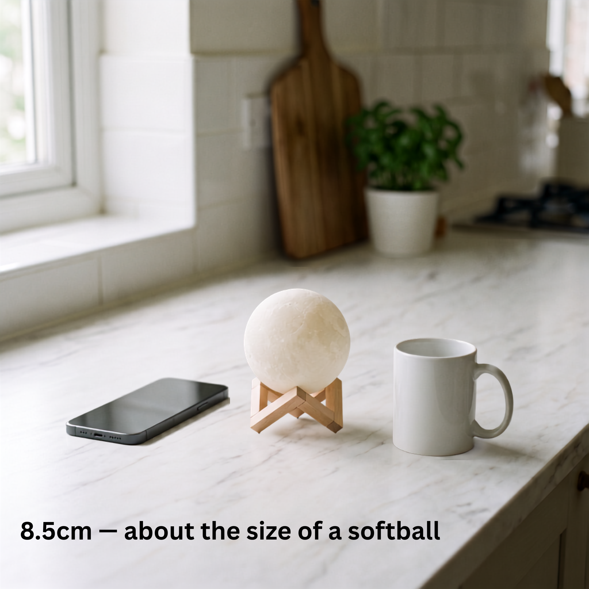 Luna moon lamp on a kitchen counter beside a phone and mug, shown at 8.5 cm, about the size of a softball