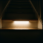 Nook Light motion sensor bar lighting a dark wooden staircase from under a step