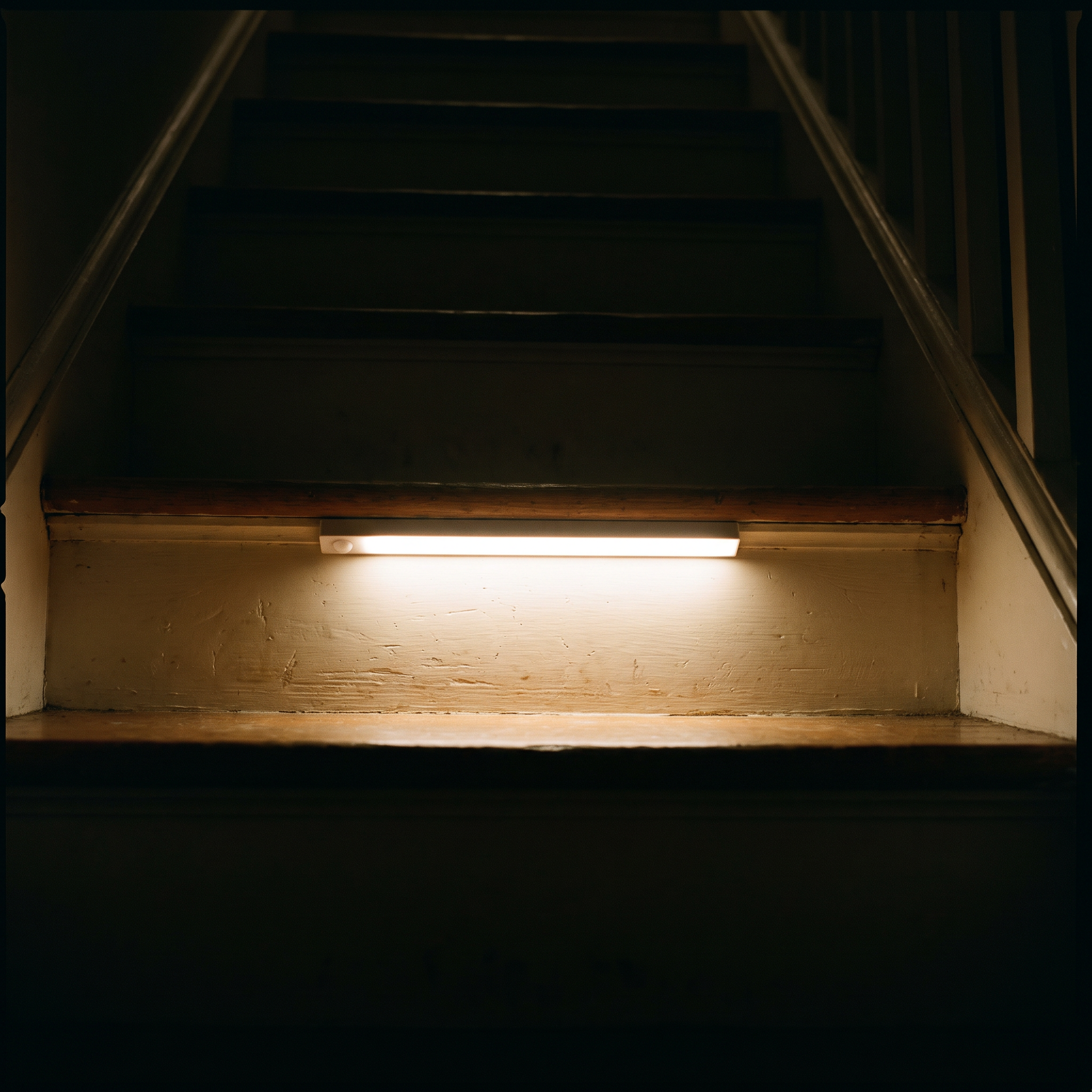 Nook Light motion sensor bar lighting a dark wooden staircase from under a step