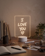 NoteGlow message board glowing on a desk beside an open notebook, pen and houseplants