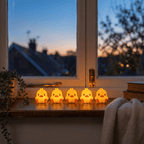 Five Peep duck night lights lined up along a windowsill at dusk with a city view behind