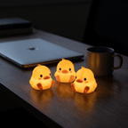 Three Peep night lights glowing on a dark desk beside a laptop and mug at night