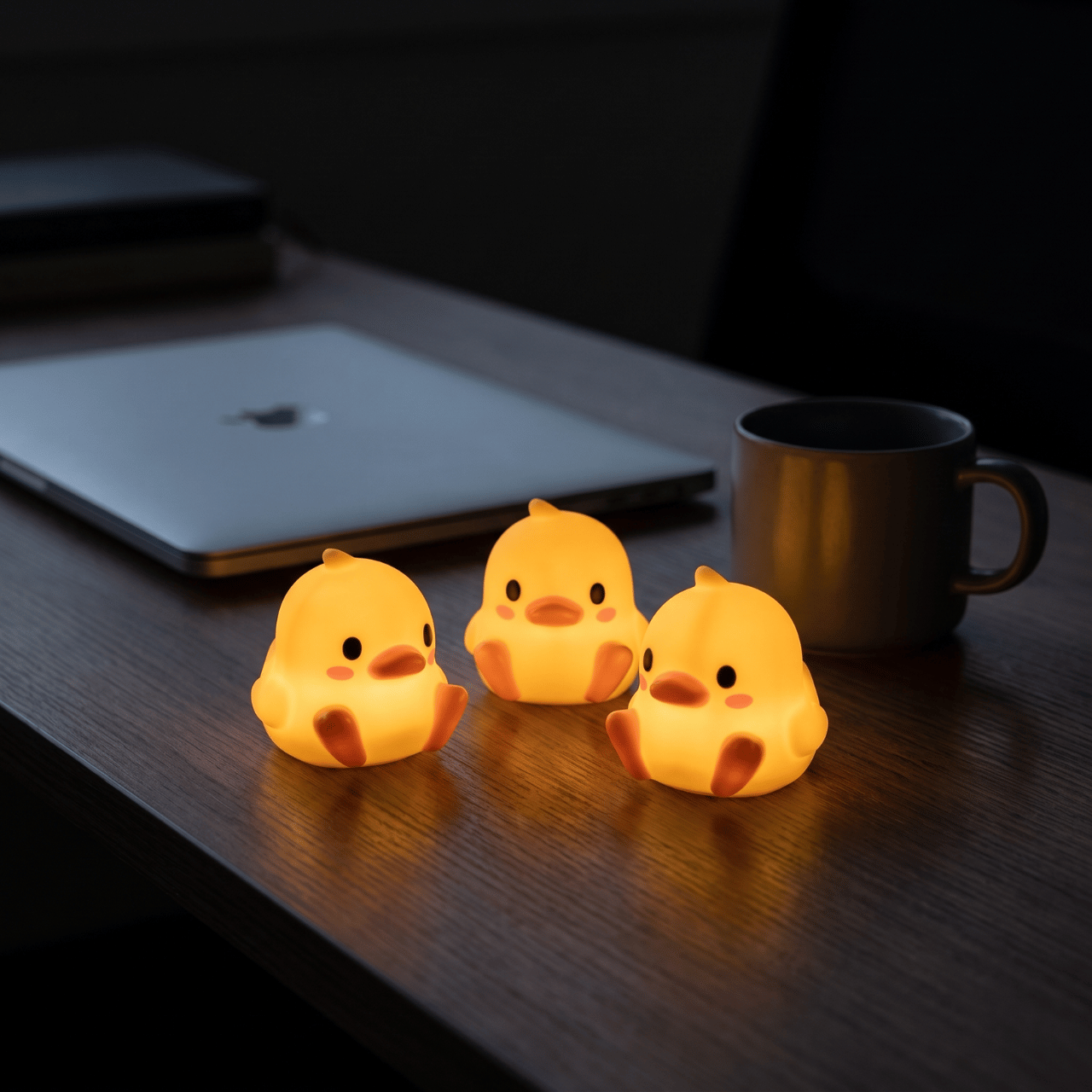 Three Peep night lights glowing on a dark desk beside a laptop and mug at night
