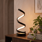 Spira spiral lamp glowing on a wooden console beside a plant and stacked design books
